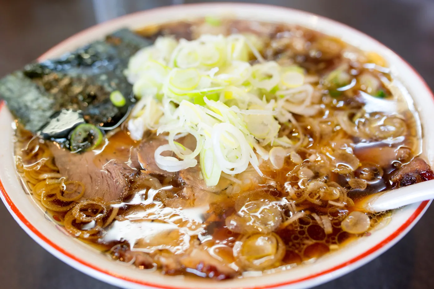 A bowl of Nagaoka-style ginger soy sauce ramen from Aoshima Shokudo in Niigata, with sliced chashu, nori and thin-cut white onion in a clear brown broth