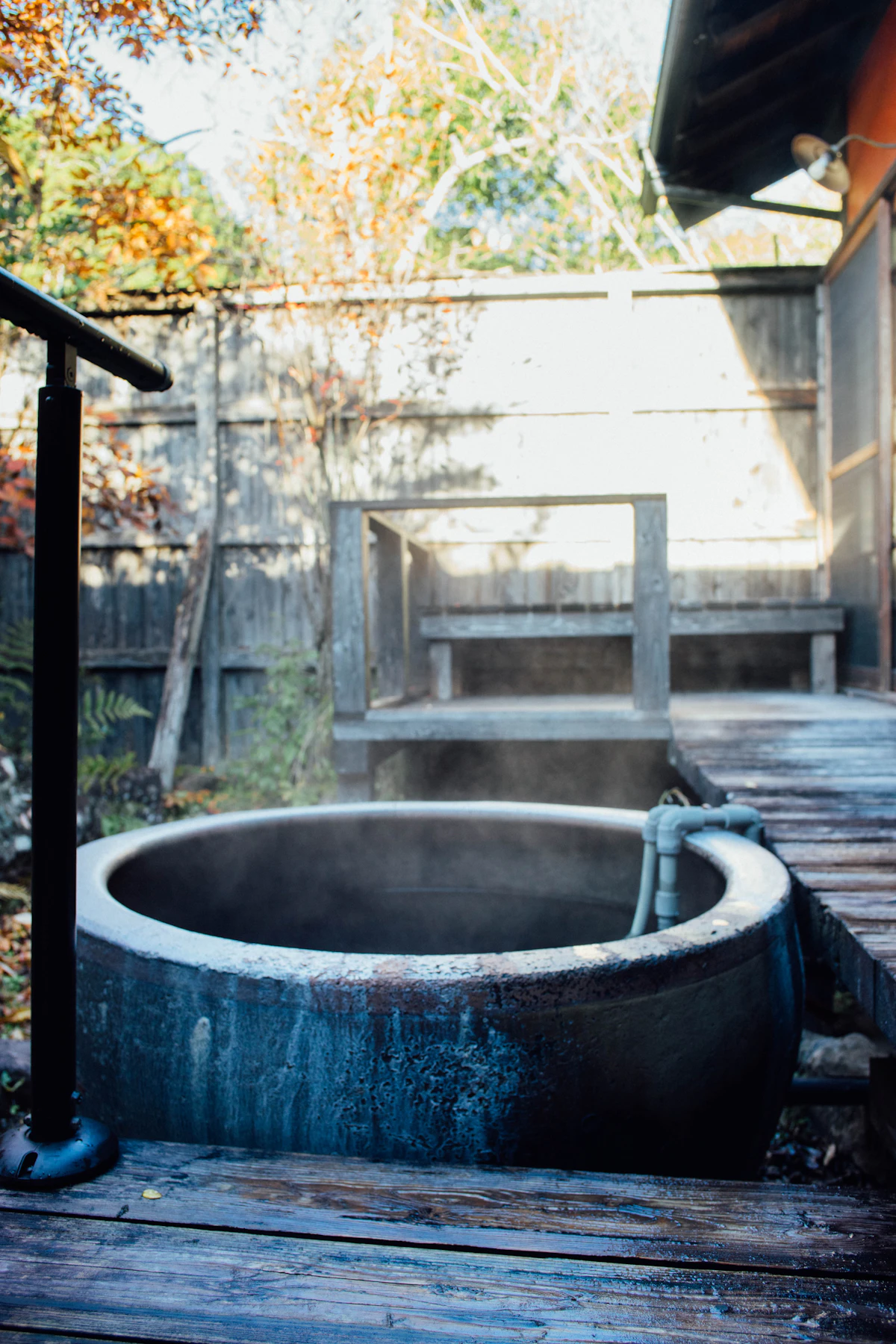 A steaming private outdoor bath on a wooden deck surrounded by autumn foliage