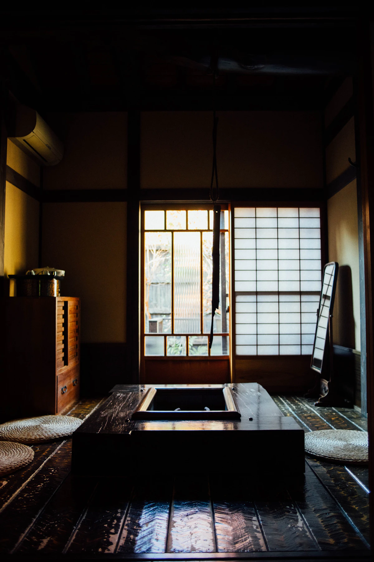 A traditional Japanese room with an irori hearth, shoji screens, and woven cushions