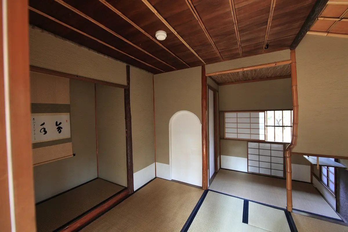 Interior of a small Japanese tea room with tatami mats, a hanging scroll in the alcove, plaster walls and a paper screen window