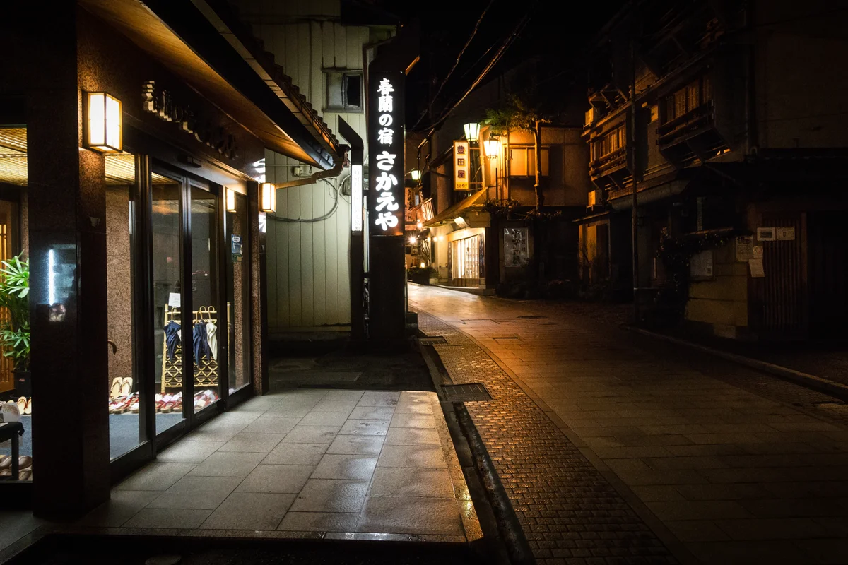 Empty stone-paved street in Shibu Onsen at night, lit by ryokan signs and lanterns
