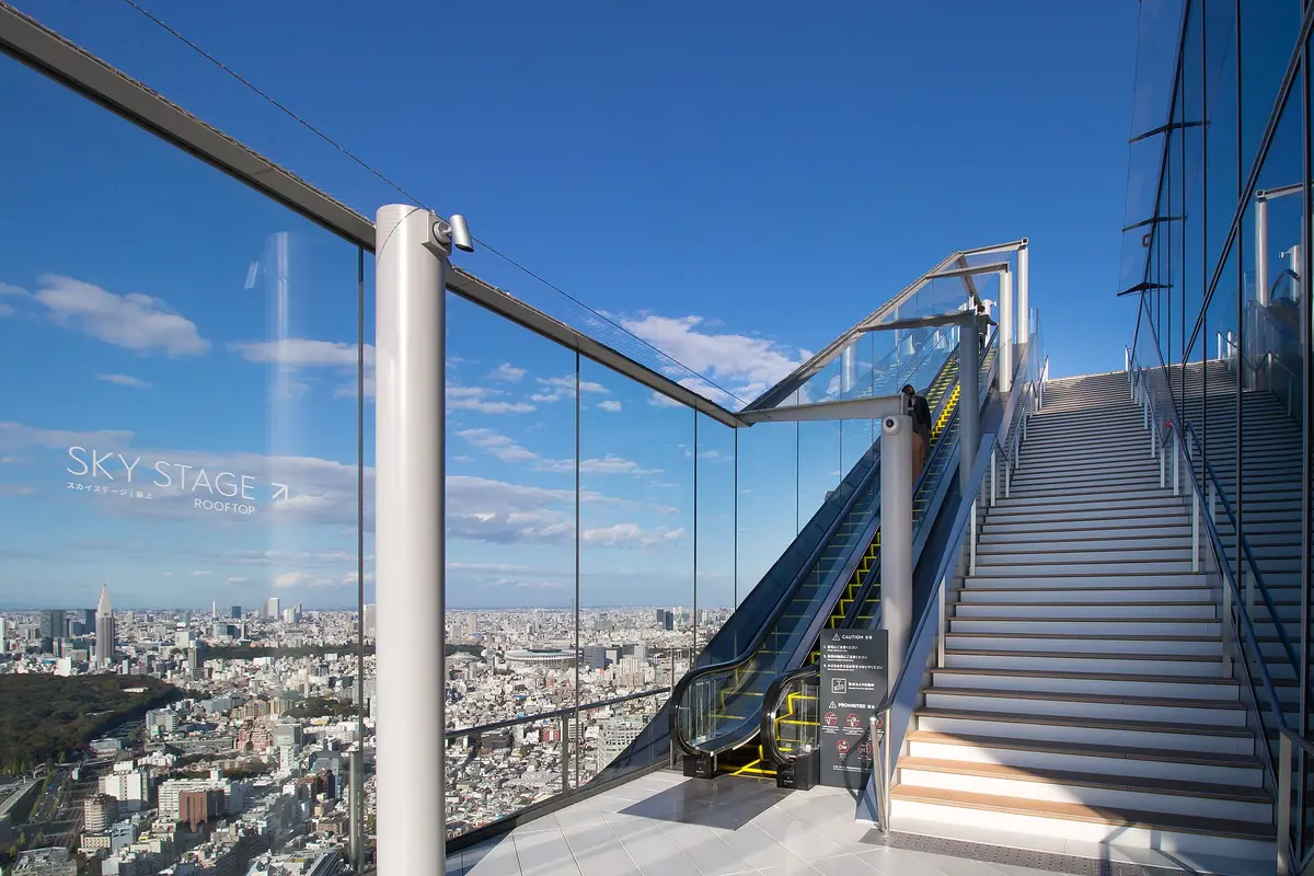 A glass-walled escalator and stairs rising to the Sky Stage rooftop at Shibuya Sky, with Tokyo spread out far below