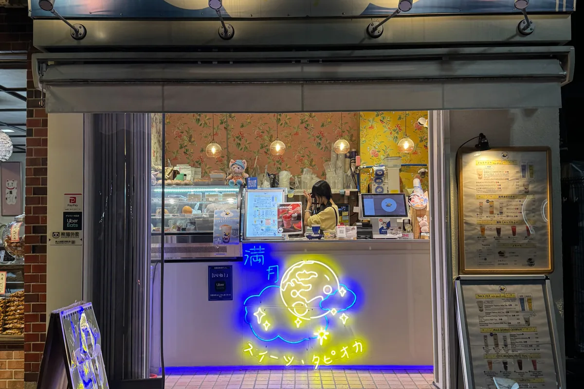 ร้านชานมไข่มุกเล็ก ๆ ที่มีป้ายไฟนีออนสว่างไสวยามค่ำคืนในชิโมคิตะซาวะ มีพนักงานกำลังทำงานอยู่หลังเคาน์เตอร์