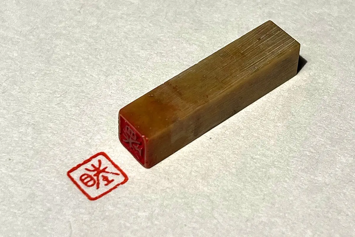 Un piccolo sigillo posato sulla carta, accanto all'impronta rossa quadrata che ha appena lasciato