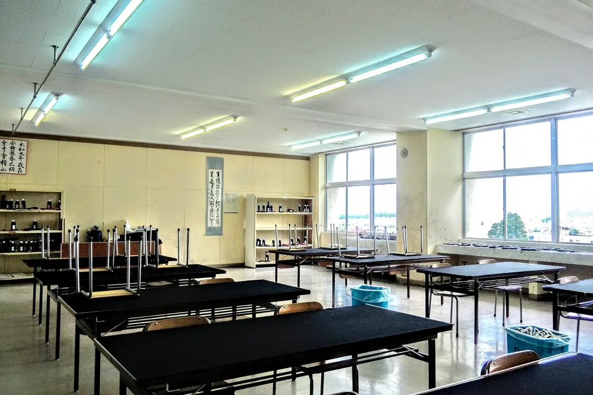 Un'aula di calligrafia vuota in una scuola giapponese, con tavoli dal piano nero, boccette di inchiostro su scaffali aperti e un rotolo appeso alla parete