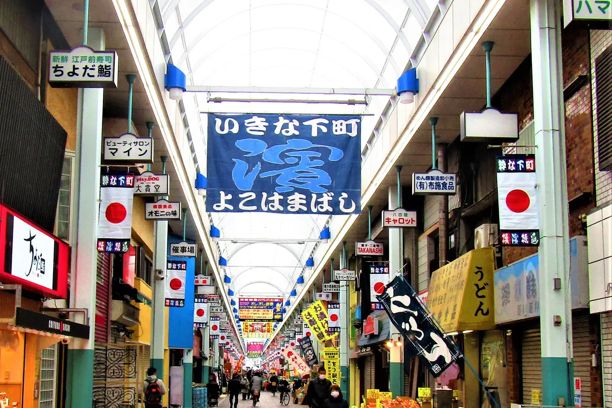 A covered shopping street under an arched roof, lined with small shops and hanging signboards