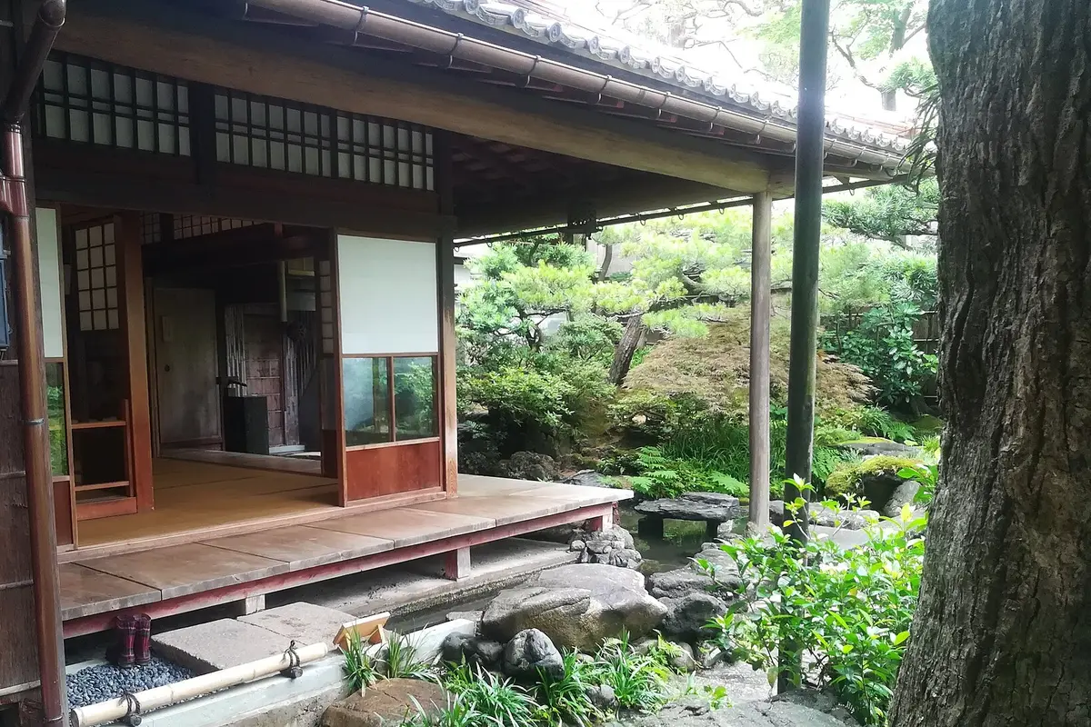 A raised wooden veranda under deep eaves, its sliding doors opened onto a green garden of pines and moss