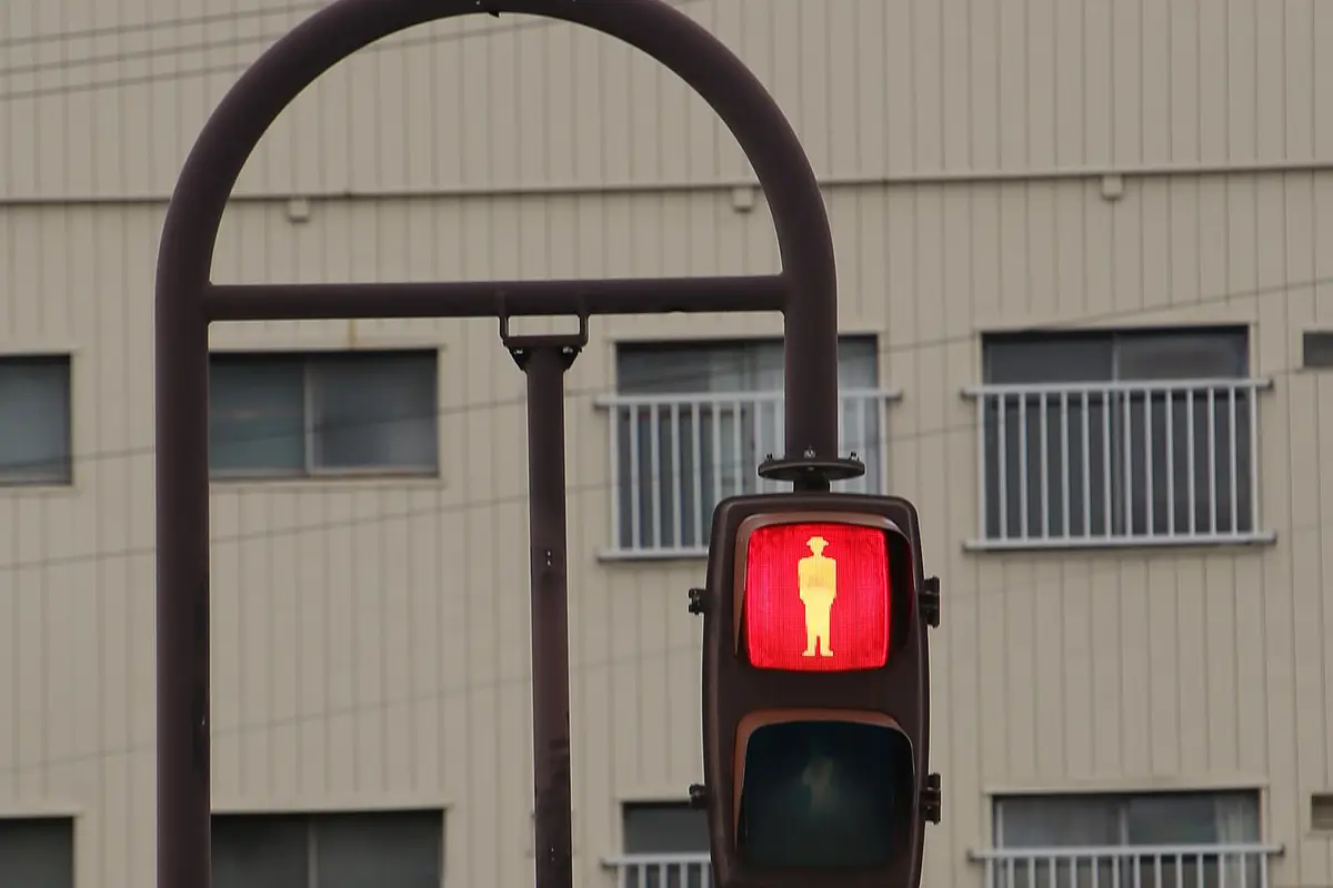A pedestrian signal in Japan showing the red standing figure, mounted on a curved arm over a city street