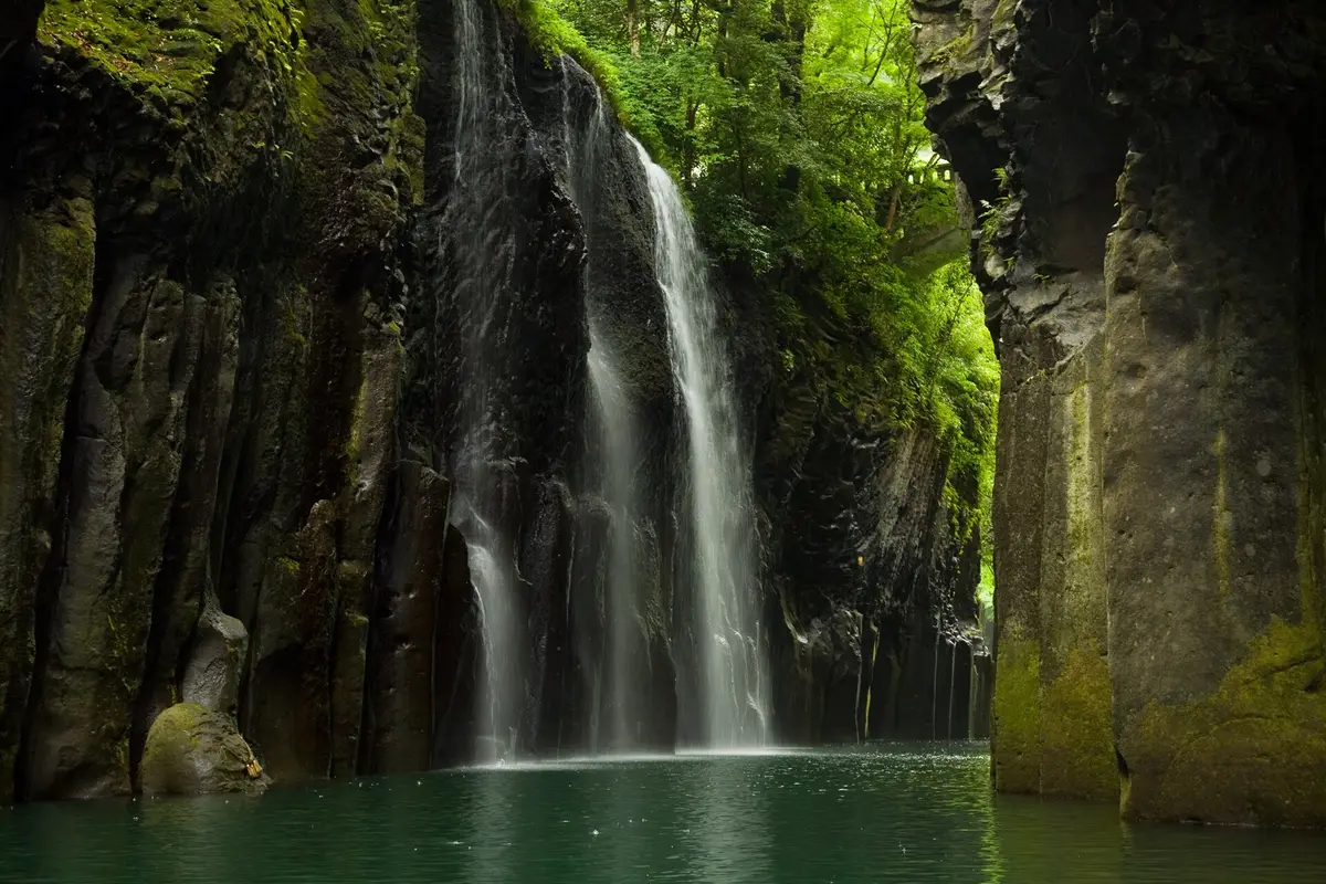 Seen from the surface of the river: Manai Falls plunging between sheer walls of dark columnar rock in Takachiho Gorge