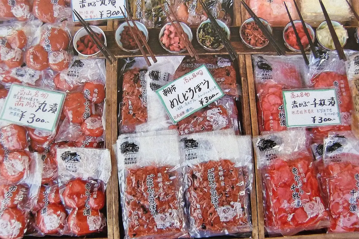 Trays of red-turnip pickles on a Takayama morning-market stall, with small tasting dishes and chopsticks set out above them