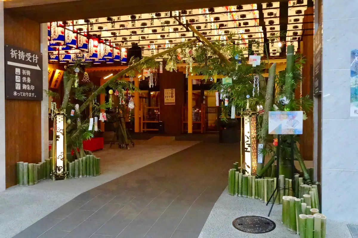 Tall fresh bamboo set up at a lantern-lit temple entrance, with small tanzaku strips tied among the leaves