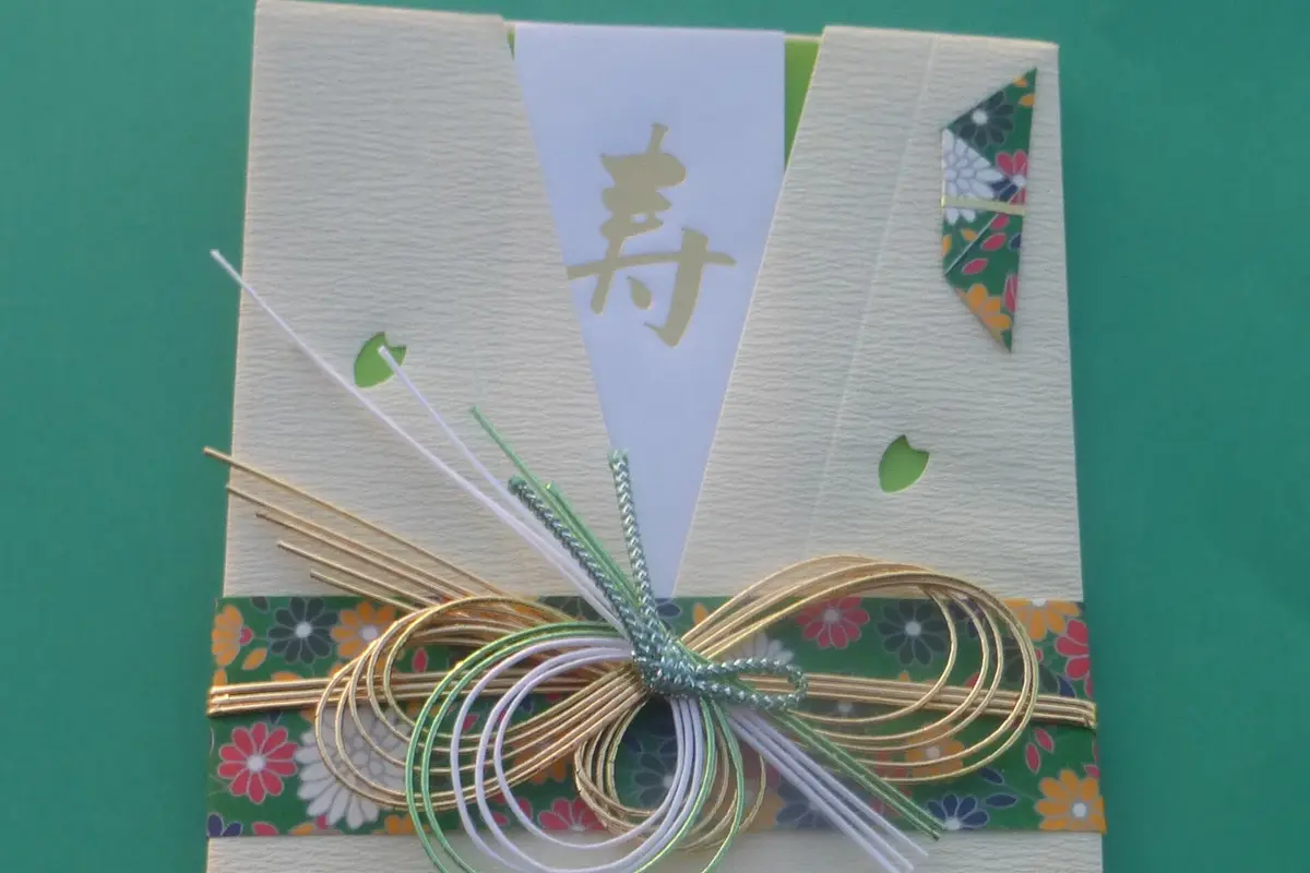 Ein japanischer Papierumschlag aus geprägtem Papier, mit goldenen, weißen und grünen Mizuhiki-Schnüren zu einem Zierknoten gebunden
