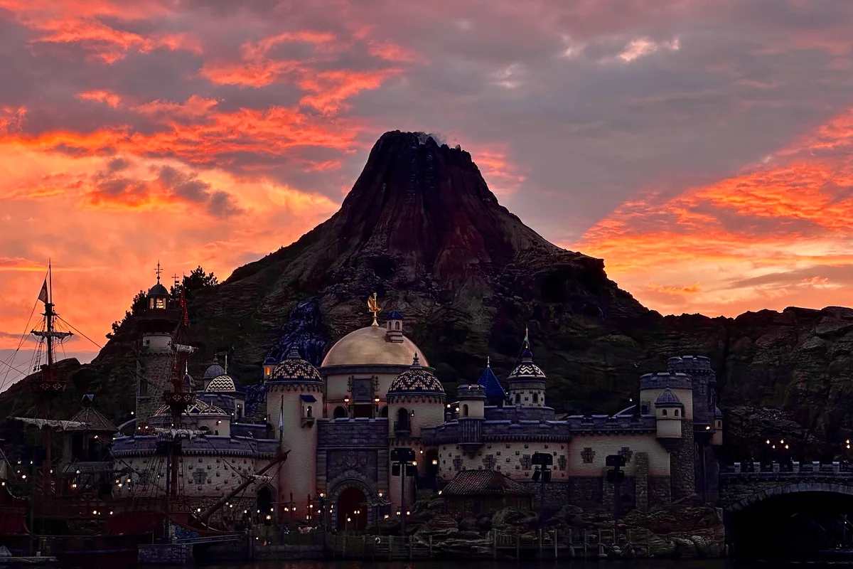 Mount Prometheus volcano at Tokyo DisneySea silhouetted against a dramatic orange sunset sky, with the Mediterranean Harbor below