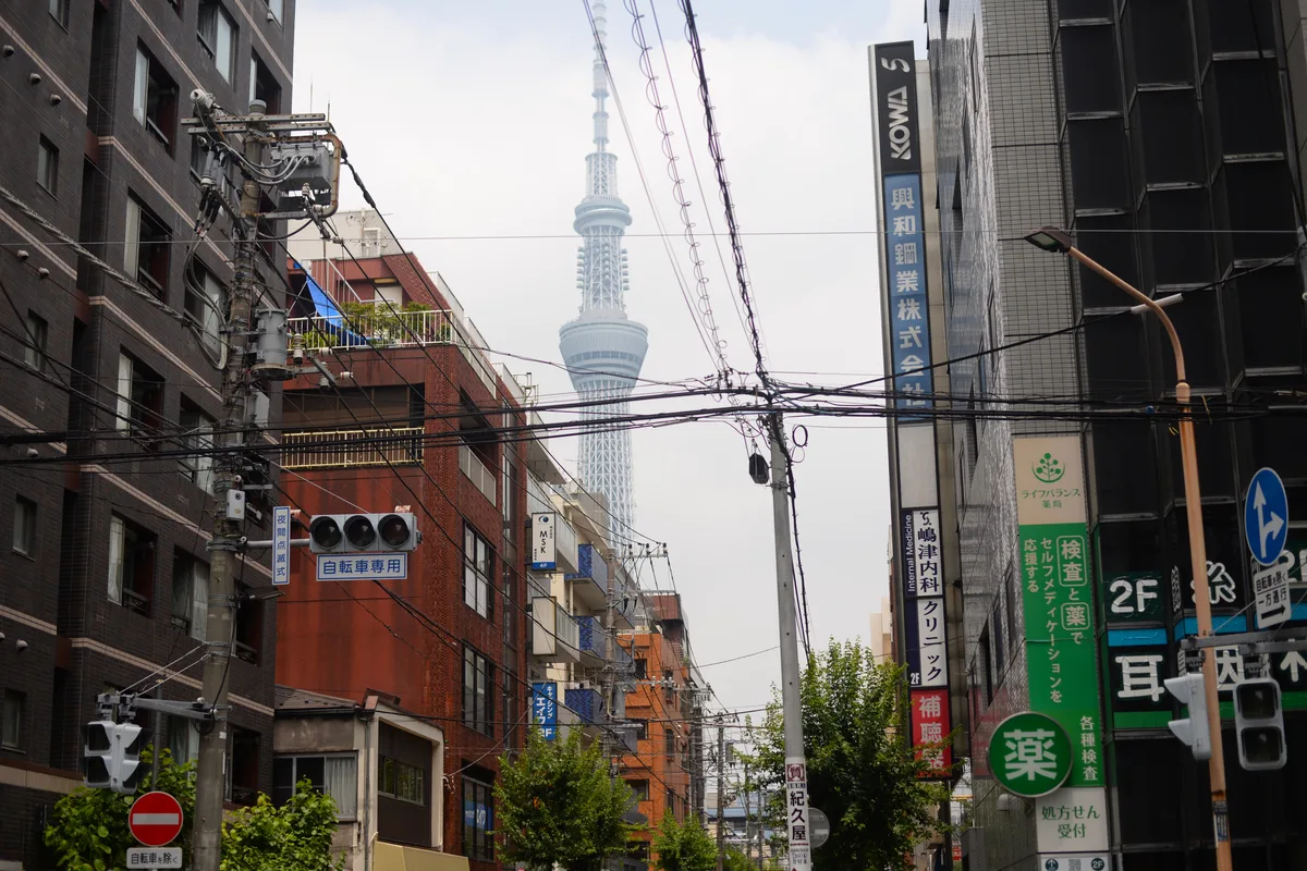 Tokyo Skytree seen rising above an ordinary Tokyo side street, framed between apartment buildings and power lines