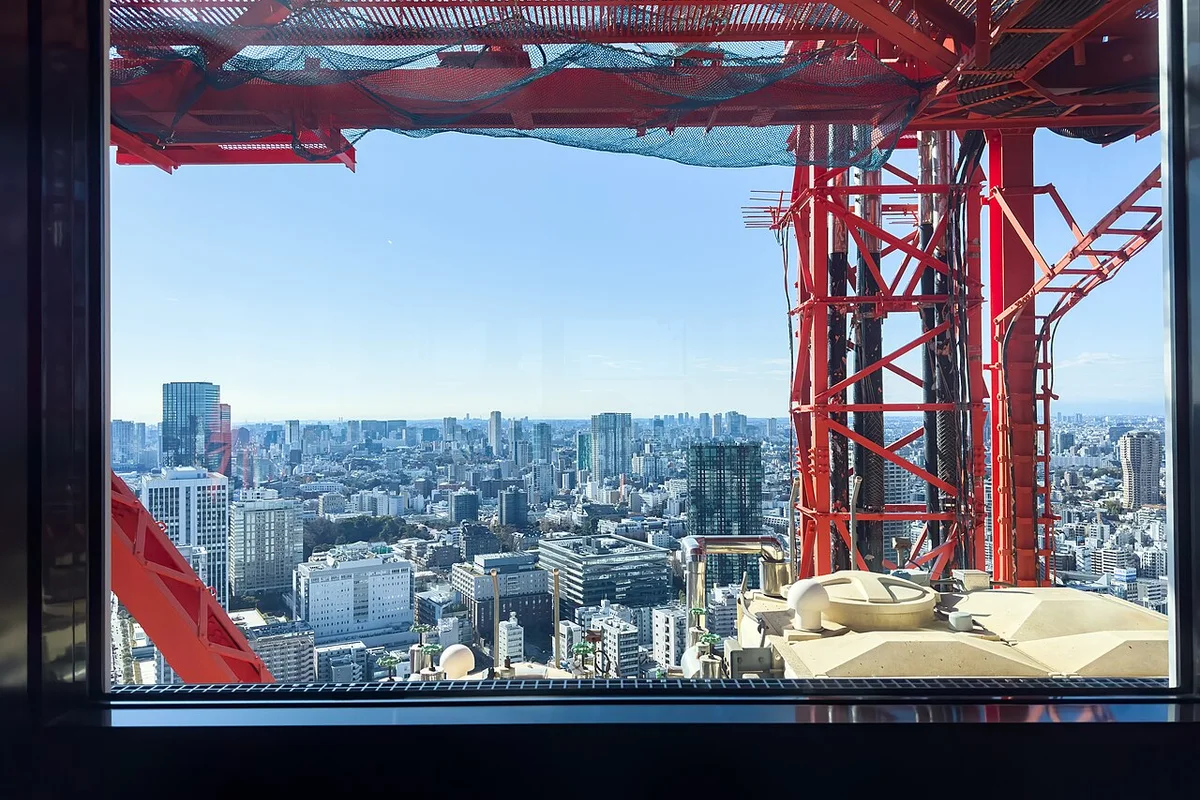 Vista a través de una ventana cerca de la cima de la Torre de Tokio, más allá de su propia estructura de acero rojo y de la red de seguridad, hacia el denso horizonte de Tokio muy abajo