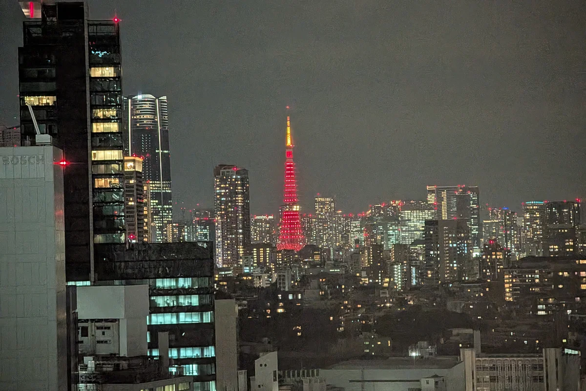 La Torre de Tokio iluminada en rojo, vista desde la distancia y empequeñecida por las siluetas oscuras de los rascacielos que la rodean de noche