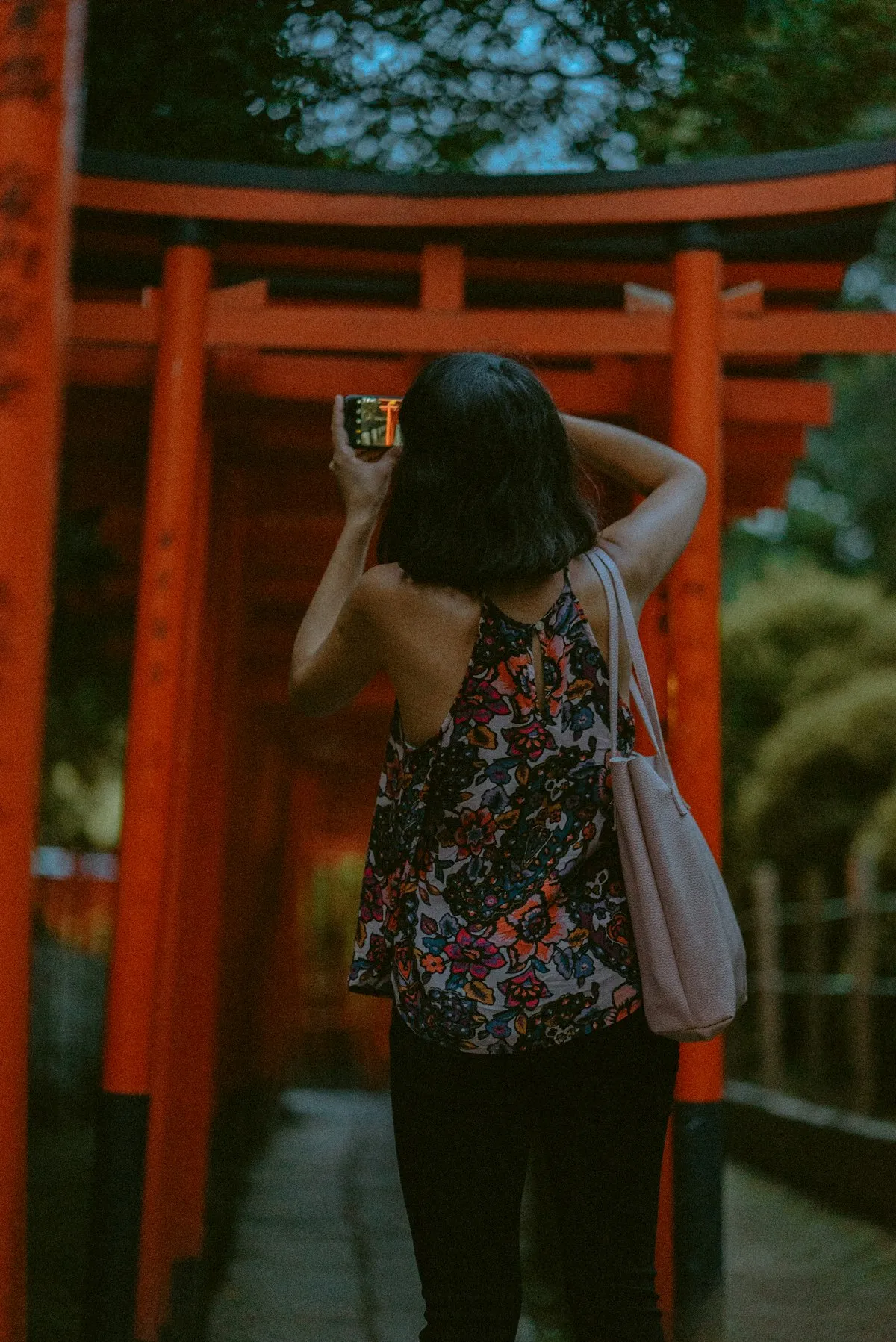 A woman photographing red torii gates with her smartphone at a Japanese shrine