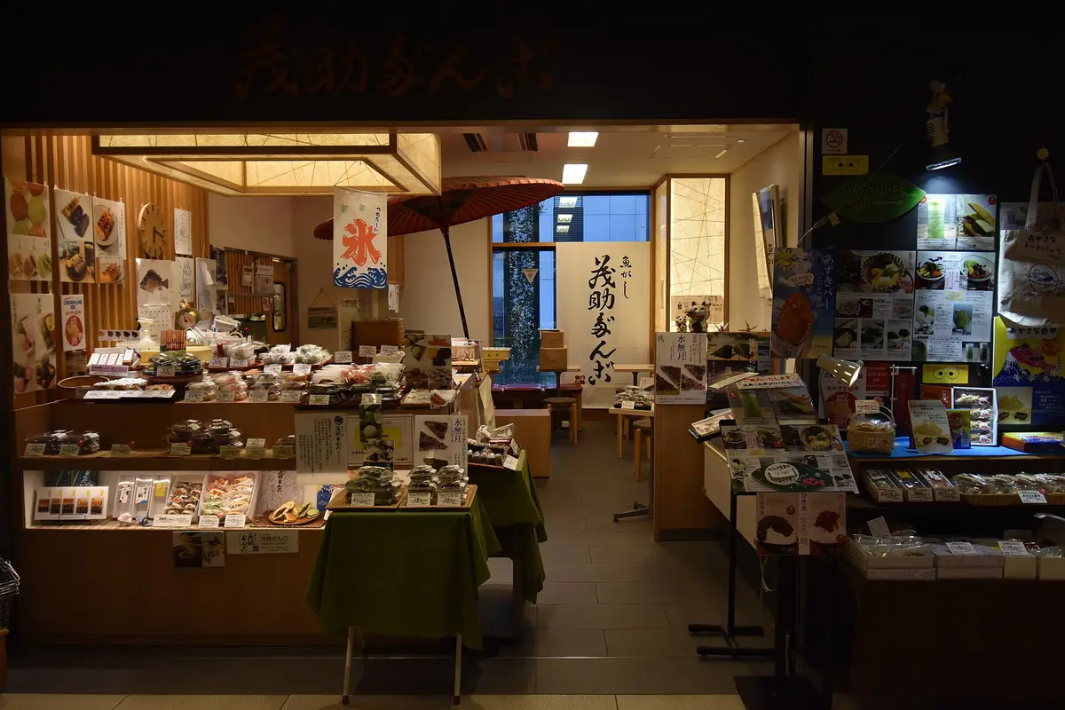A sweet shop counter inside the Toyosu market building, with trays of wrapped sweets, a red paper parasol and a hand-lettered shop banner