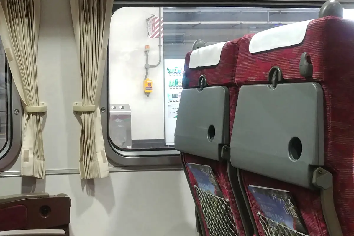 Rows of seats with folded tray tables and white headrest covers inside a Japanese limited express carriage