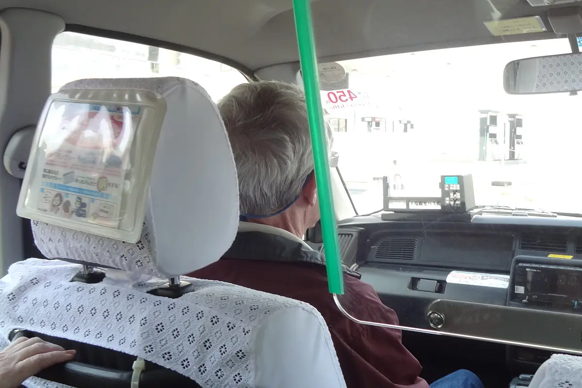 The view from the back seat of a Japanese taxi, with lace-covered seats and the fare meter on the dashboard ahead