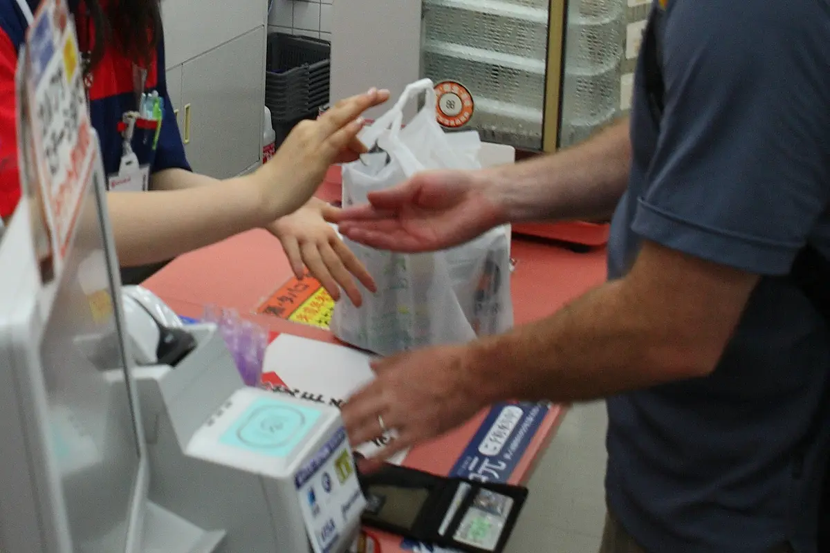 Hands over a convenience store counter: a plastic bag is passed across and another pair of hands reaches out to take it