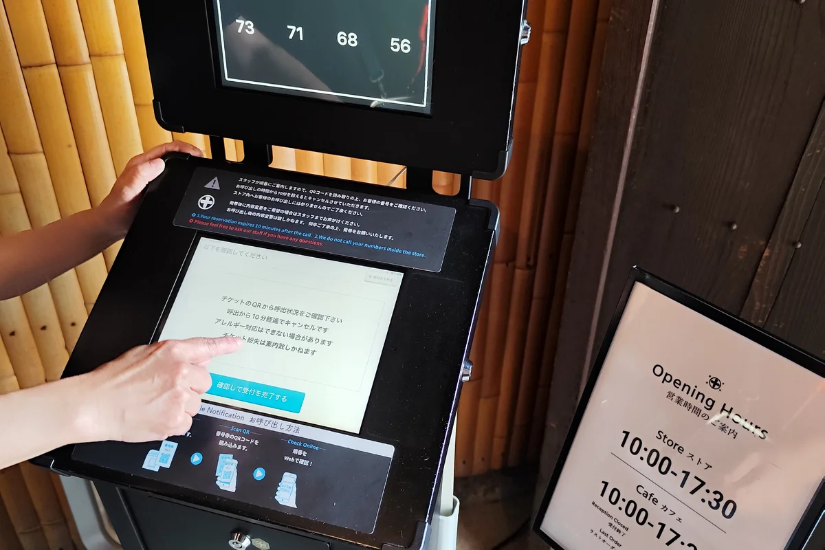 Un display digitale dei numeri di attesa in una casa da tè di Uji, che mostra decine di gruppi ancora in coda, accanto a un cartello stampato con gli orari di apertura del negozio