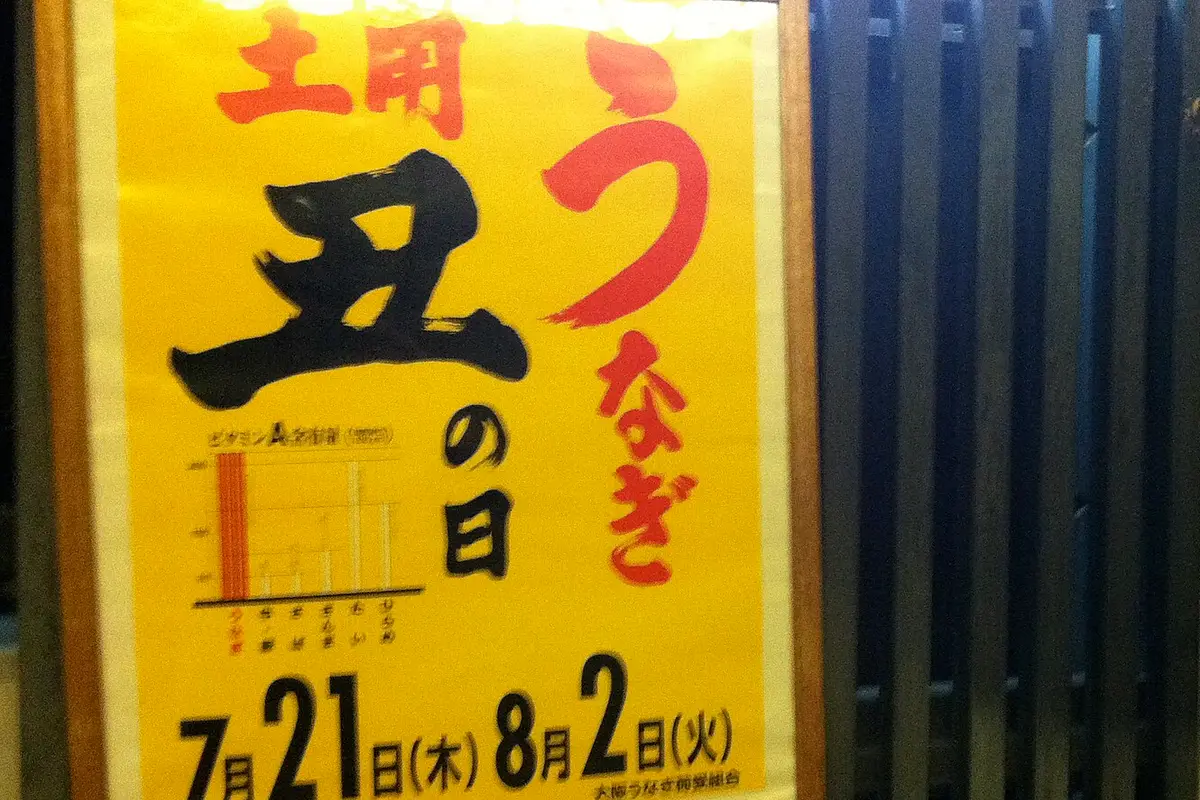 A framed shop poster in brush lettering reading Doyo Ushi no Hi and unagi, with two summer dates printed along the bottom