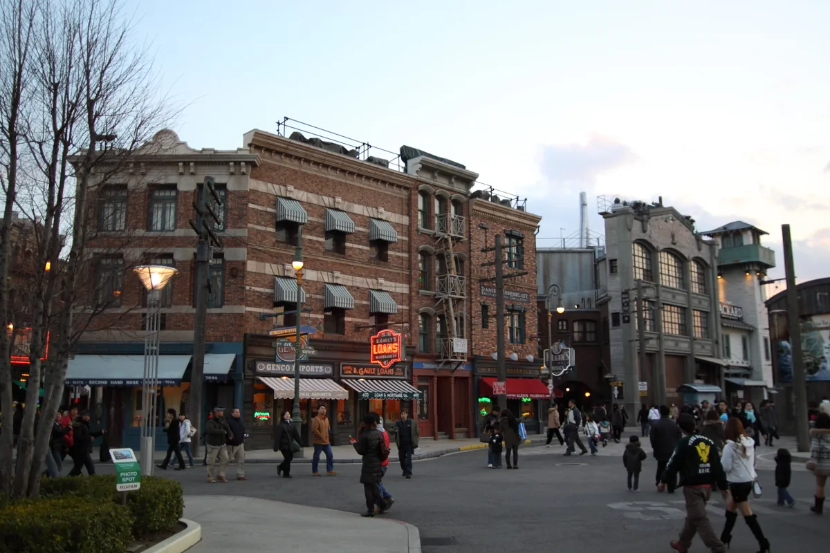 The recreated New York backlot street at dusk, brick facades and neon shop signs lit against a darkening sky, visitors strolling below