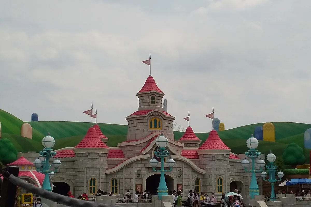 Peach's Castle in Super Nintendo World, its pastel turrets rising against the painted green hills, with a small queue gathered at its gates