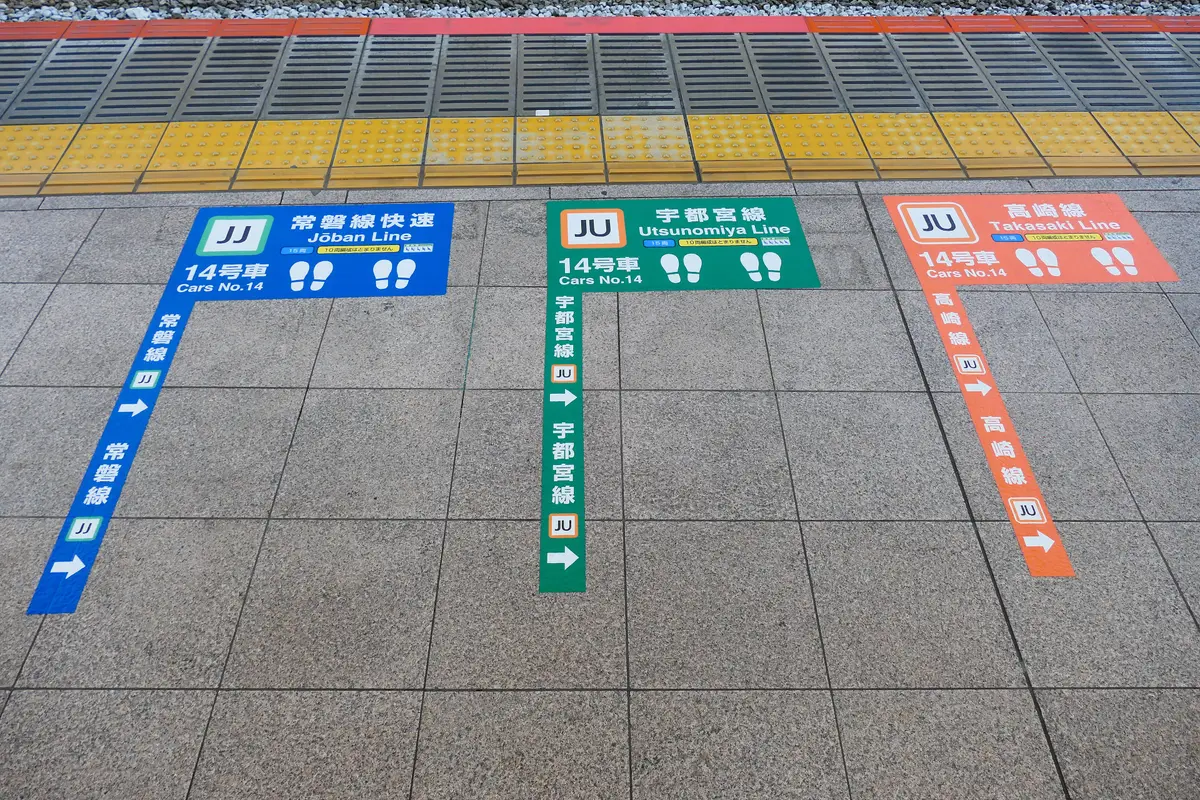 Painted boarding markings on a station platform in Tokyo, with footprint symbols and the names of three train lines