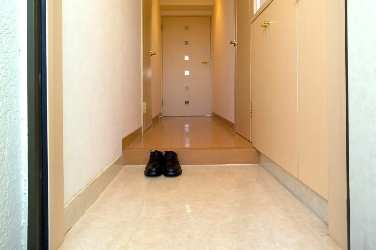 A single pair of shoes on the tiled entrance floor of a Japanese home, in front of the raised step leading up to the wooden indoor floor