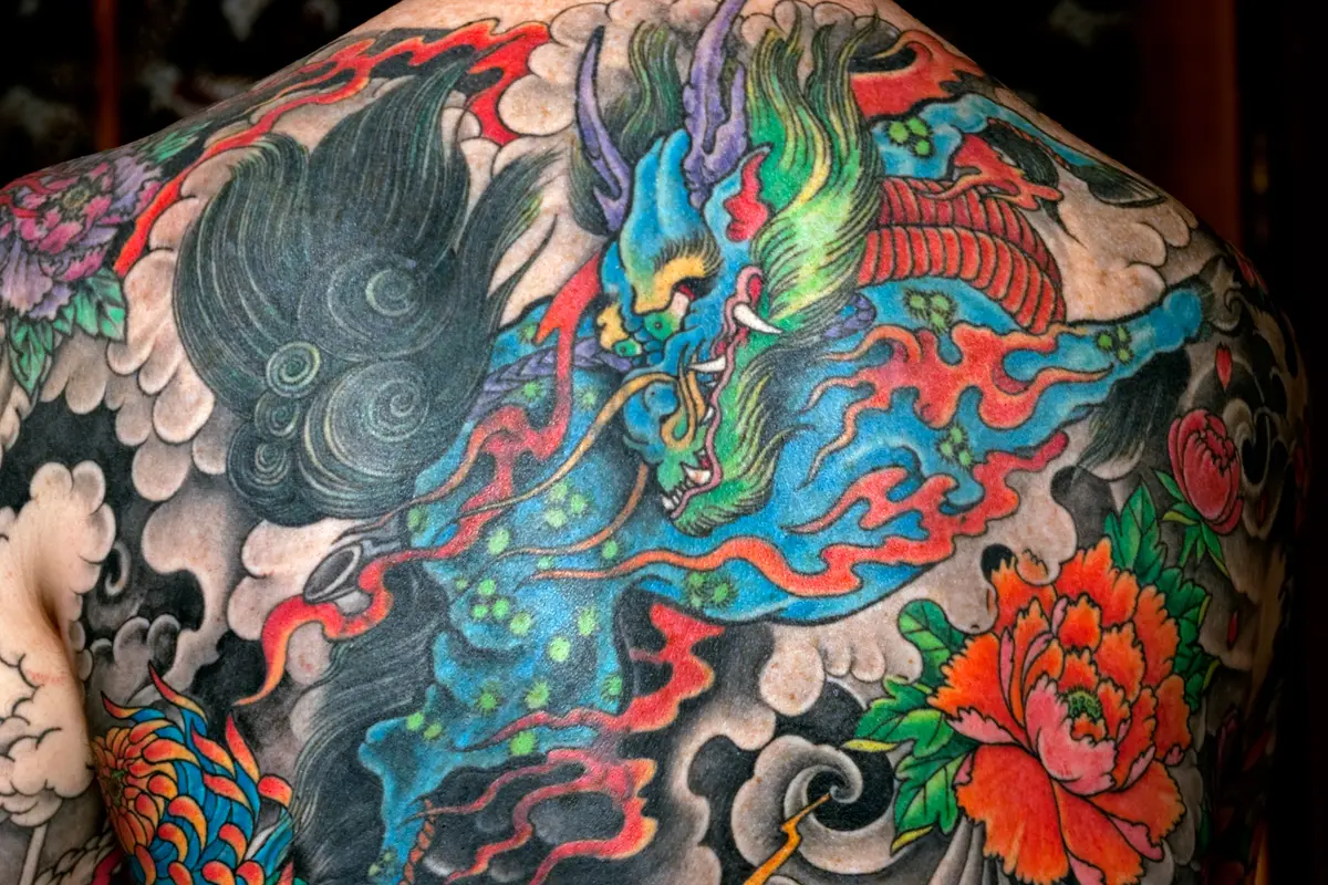 Ein vollständig tätowierter Rücken im japanischen Stil: ein Drache zwischen Wolken, dazu Pfingstrosen und Chrysanthemen