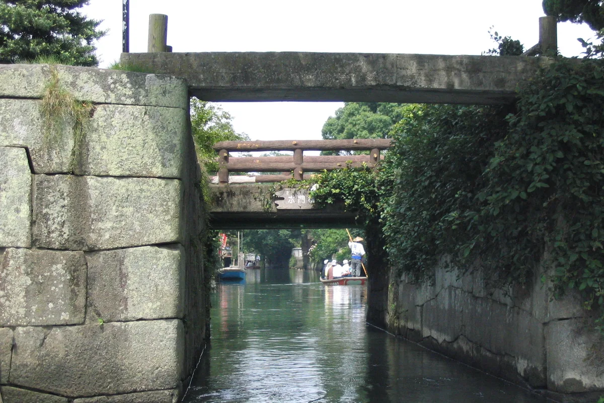 View from a canal boat approaching a very low stone bridge, with a donko-bune boat passing under it ahead