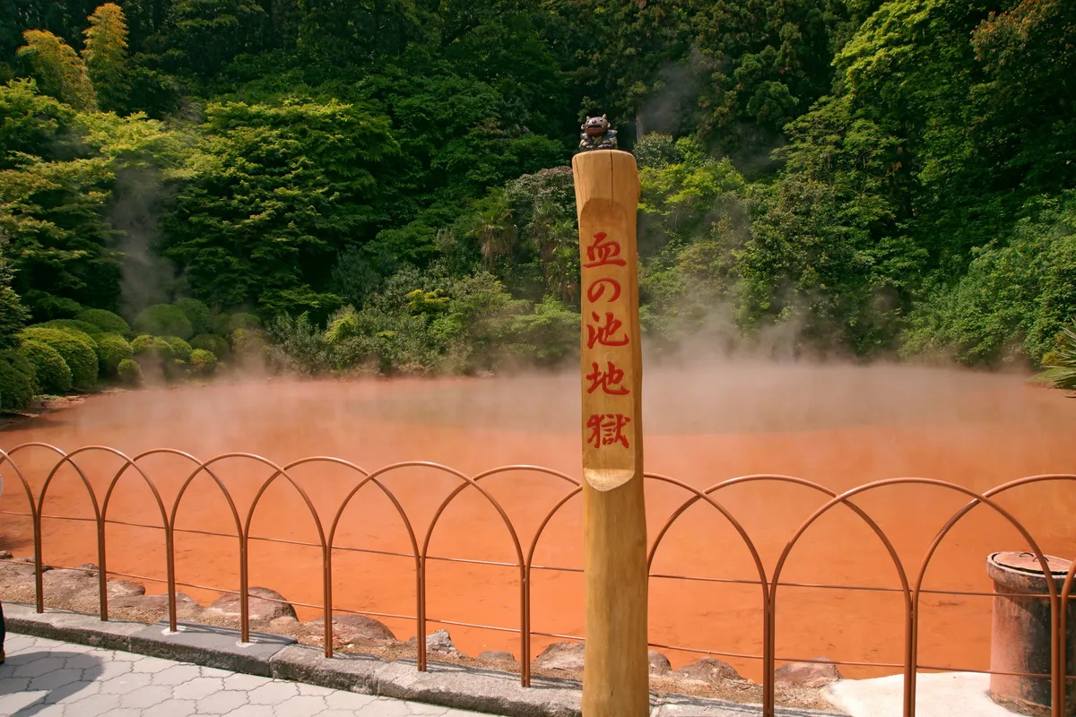 Chinoike Jigoku, the "blood pond hell" of Beppu — scalding red water steaming behind a low viewing rail