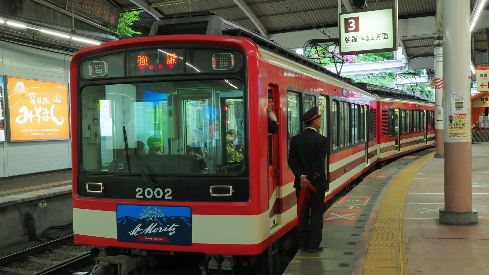 A red Hakone Tozan mountain train waiting at a platform, with a conductor standing by the open door