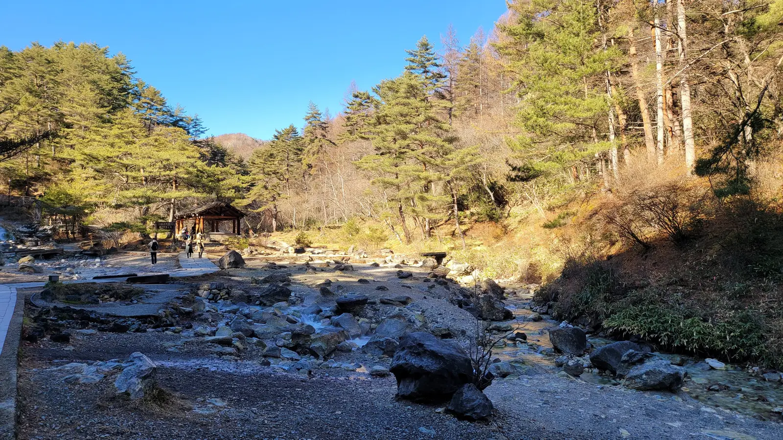 A warm stream running between rocks and pine trees in Sainokawara Park, Kusatsu, on a clear autumn day
