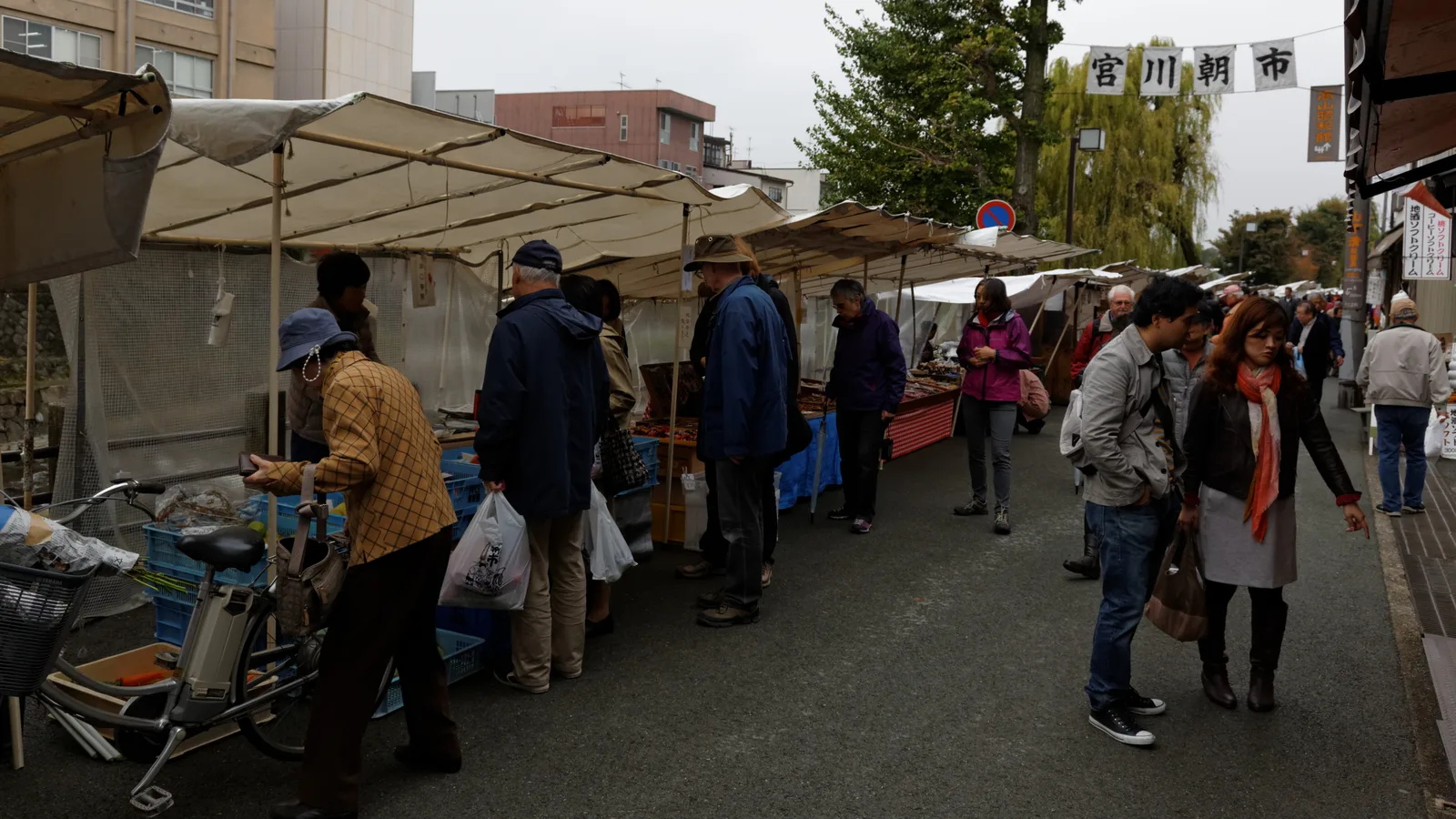 Wooden stalls of vegetables and pickles along a riverside morning market in a Japanese mountain town