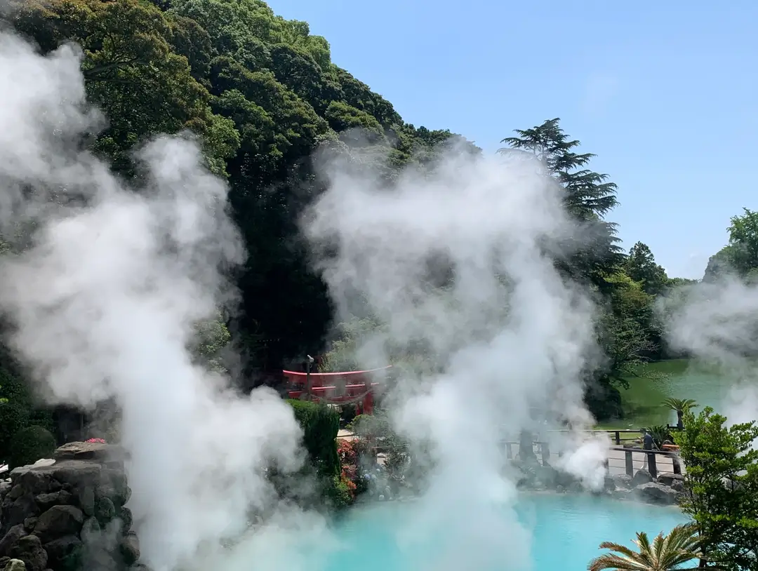 Steam pouring off the cobalt blue pool of Umi Jigoku in Beppu, with a red torii behind it