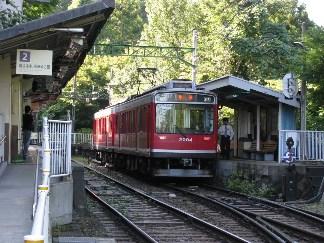 A red Hakone Tozan mountain train waiting at a small switchback station in the hills